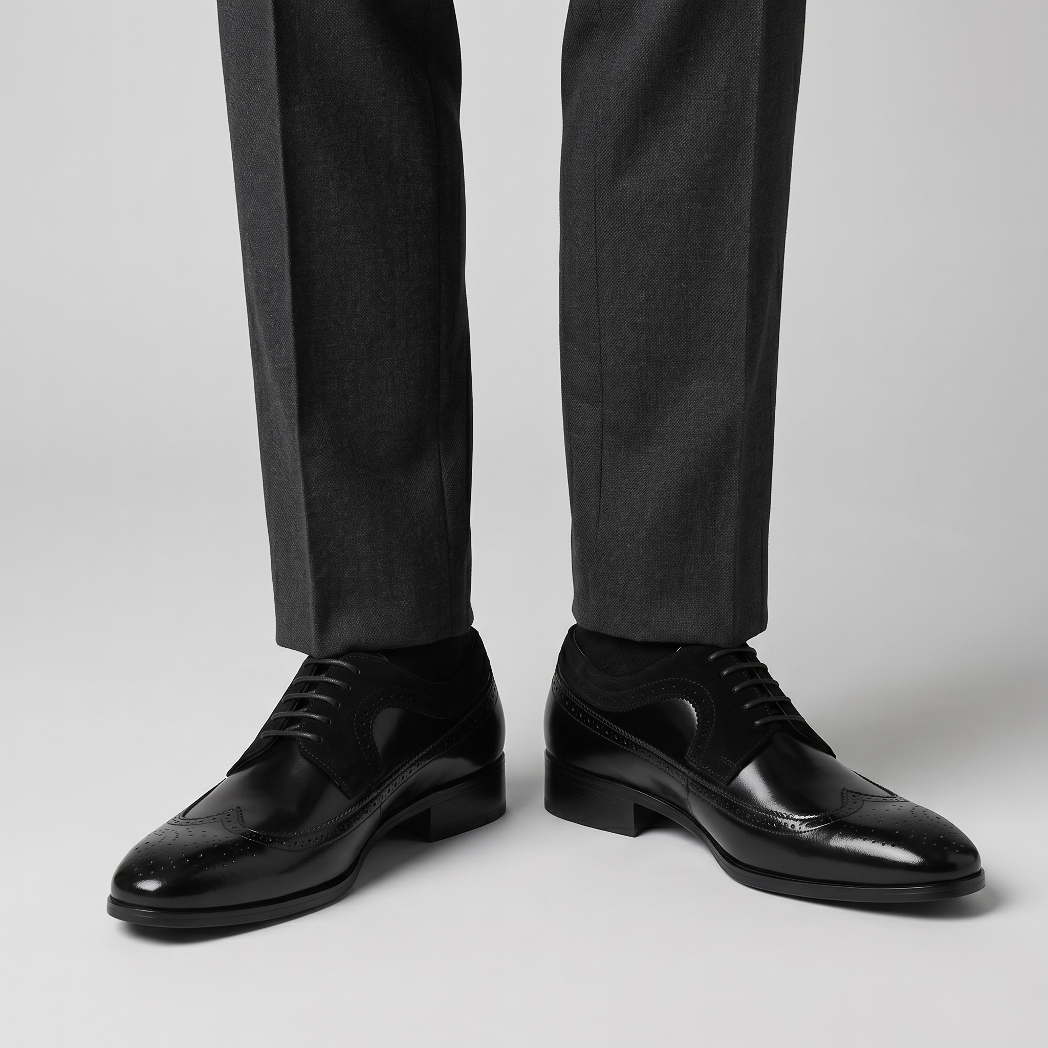 Men's black wingtip brogue Derby shoes with matte suede panels worn with charcoal trousers