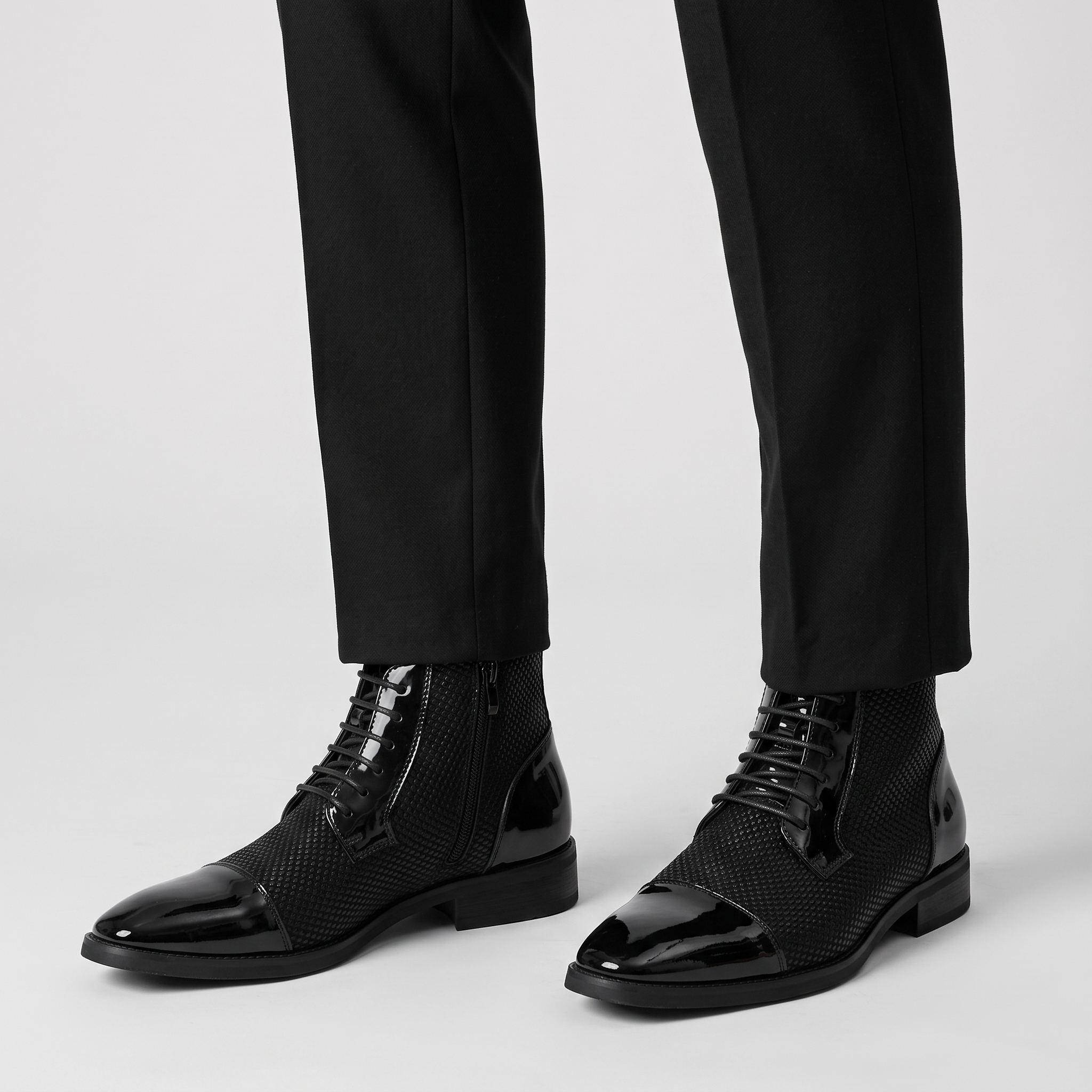Men's black patent cap toe ankle boots with textured panel worn with black trousers