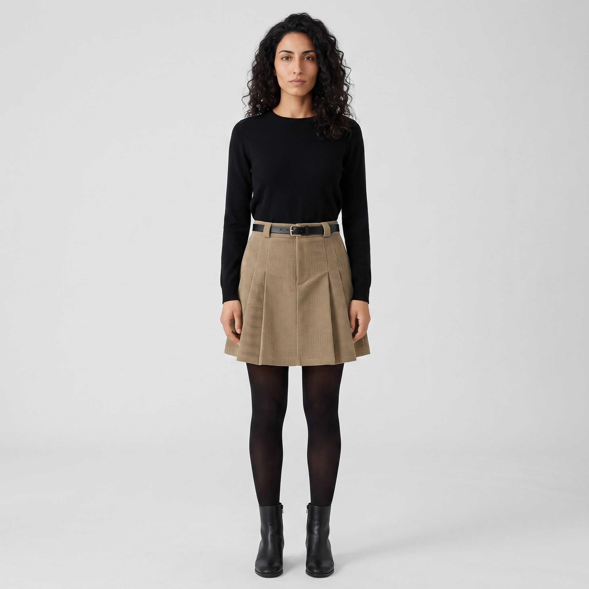Woman wearing a khaki beige pleated corduroy mini skirt with a black knit top
