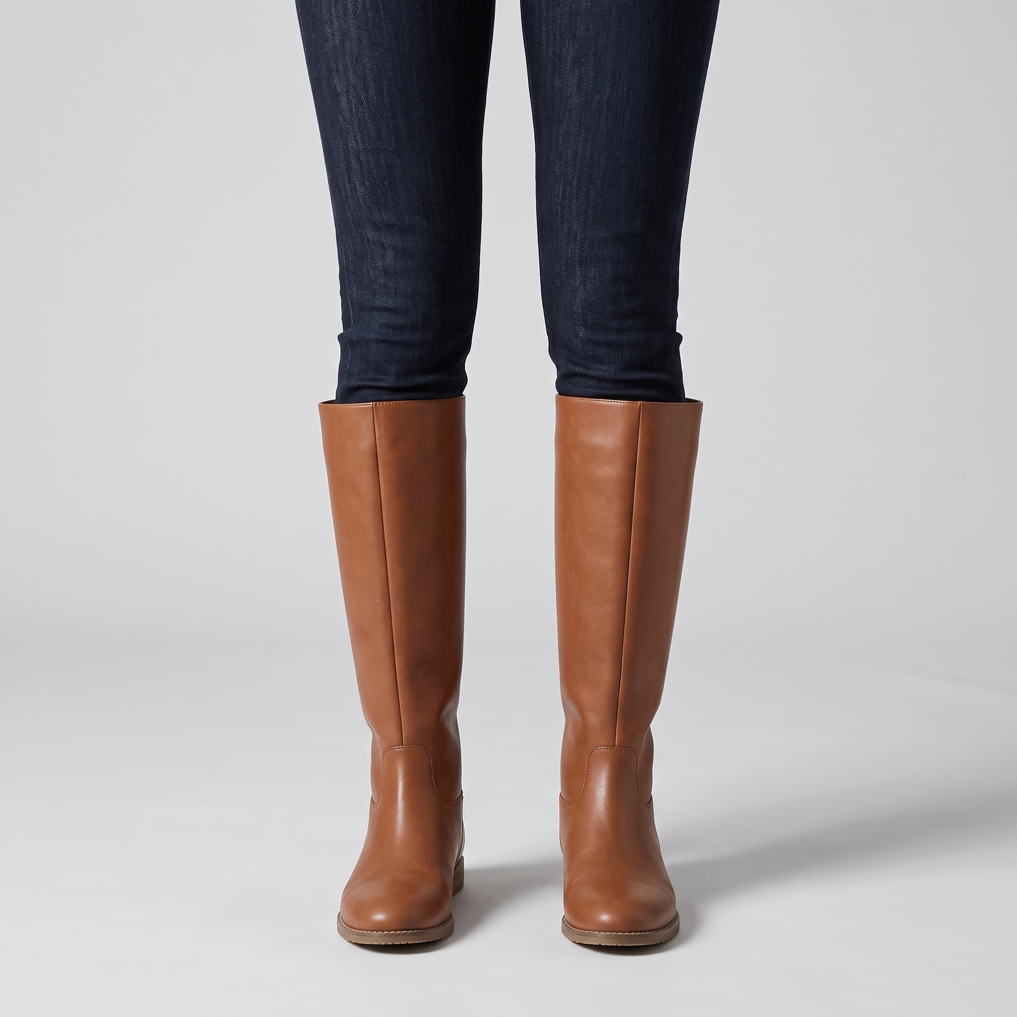 Model wearing the light brown knee high riding boots with jeans tucked in, studio shot